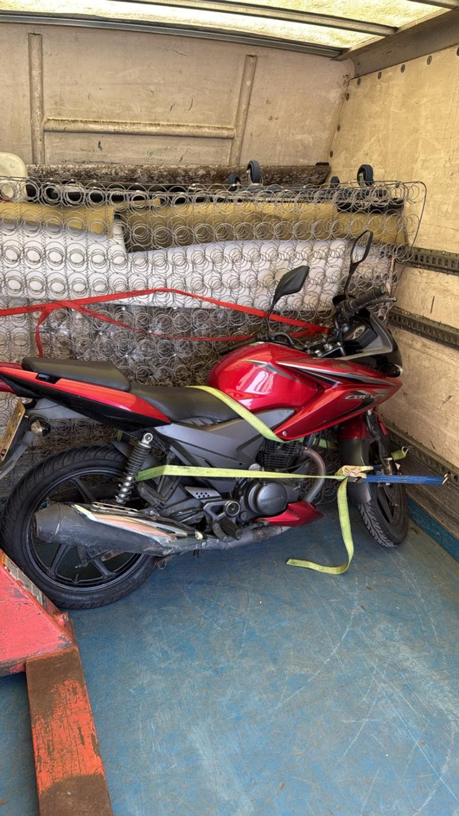 Red motorcycle strapped down and secured for transport inside a Raymond Logistics van